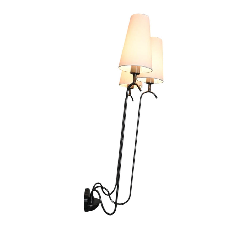 Modern three-arm wall sconce with sleek black metal frame and white fabric shades, mounted on a round base for elegant ambient lighting.