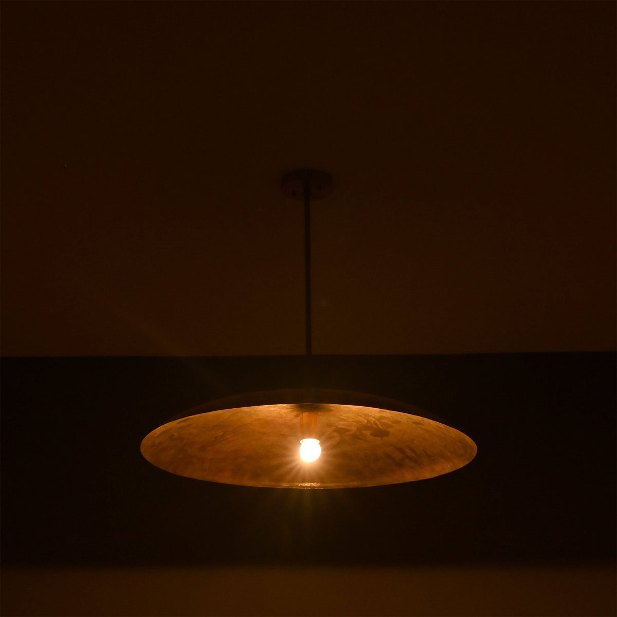 Aurelia Saucer Pendant Light glowing in a dark setting with soft downward ambient light effect.