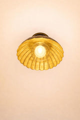Bottom view of scalloped brass flush mount ceiling light illuminated, showing warm golden reflection inside the bowl shade.
