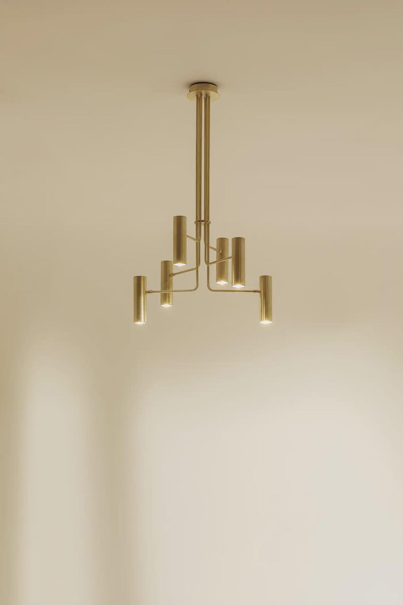 Modern brass chandelier installed on ceiling, casting warm ambient light with clean architectural lines.