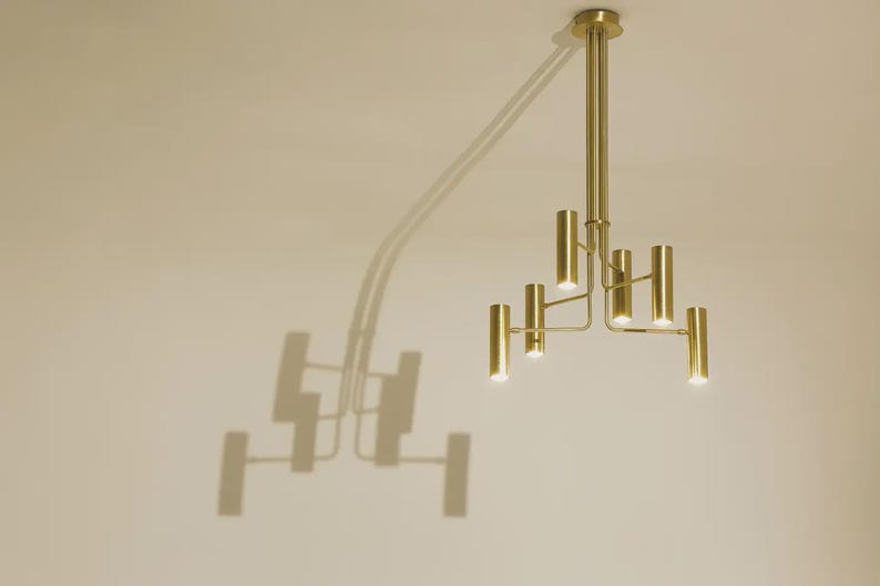 Modern brass chandelier casting artistic shadows on wall, highlighting sculptural form and architectural presence.