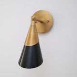 Brass and black cone wall light shown from a front-left angle with brushed brass arm and round mount.
