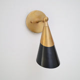 Modern two-tone cone wall sconce in brushed brass and matte black, angled view with round brass backplate.