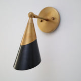Close-up angled view of brass backplate and arm with black cone shade and brass top section.