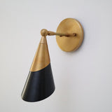 Brass and matte black cone wall sconce shown from a right-side angle with circular brass wall plate.