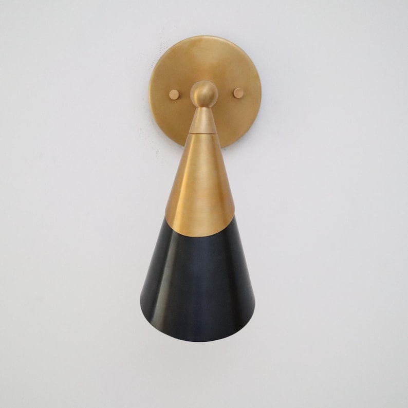 Front view of two-tone brass and black cone wall sconce with centered round brass backplate on white wall.