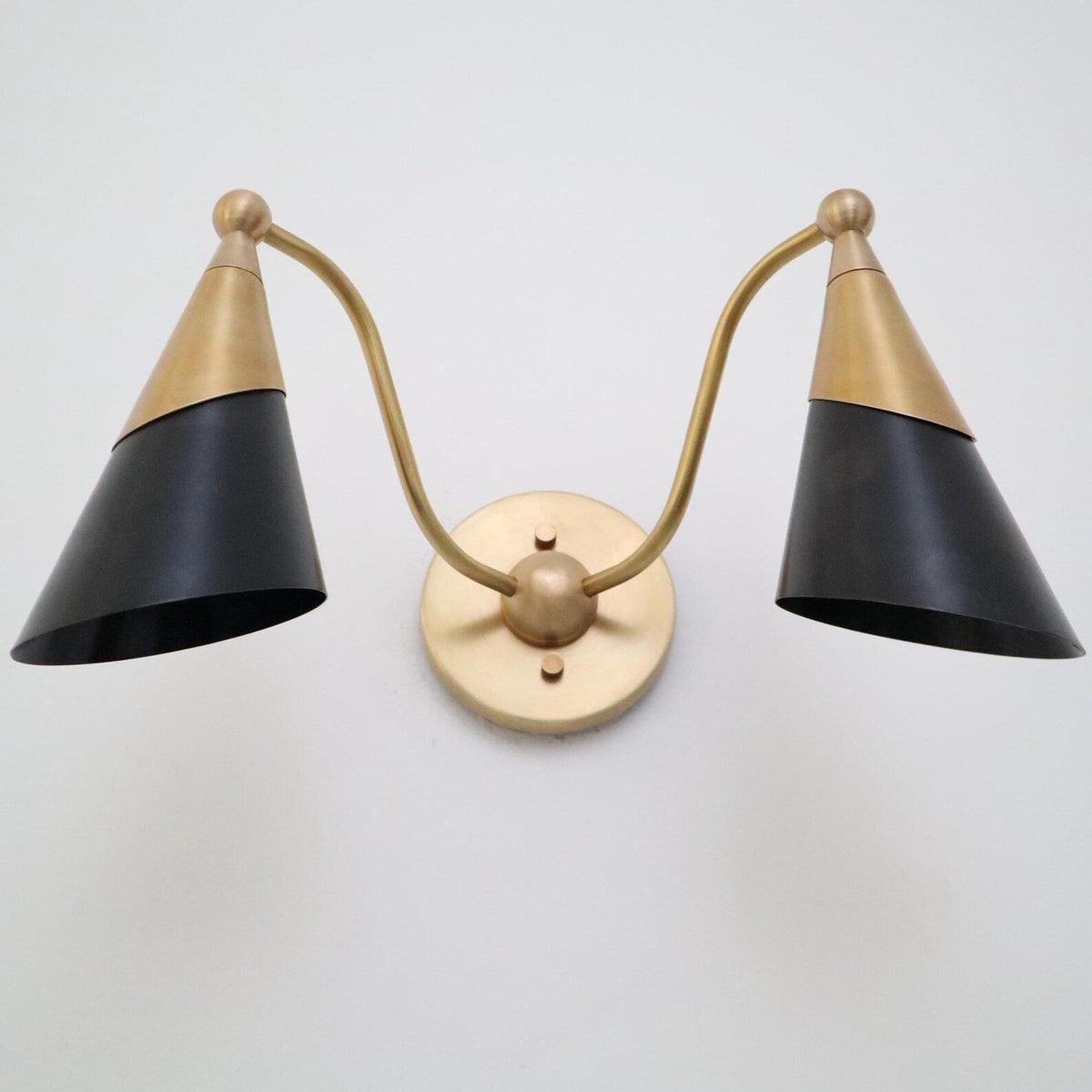 Low-angle view of a two-light brass and black cone wall sconce showing curved arms and round brass backplate.