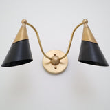 Low-angle view of a two-light brass and black cone wall sconce showing curved arms and round brass backplate.