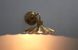 Lit brass wall sconce with scalloped disc shade casting a warm ambient glow on the wall below.