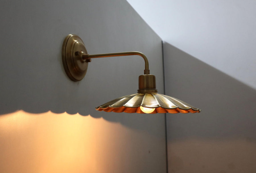 Lit brass wall sconce with scalloped disc shade casting a warm ambient glow on the wall below.