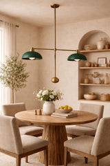 Brass double-arm pendant with green dome shades centered above a round wooden dining table in a warm neutral dining room.