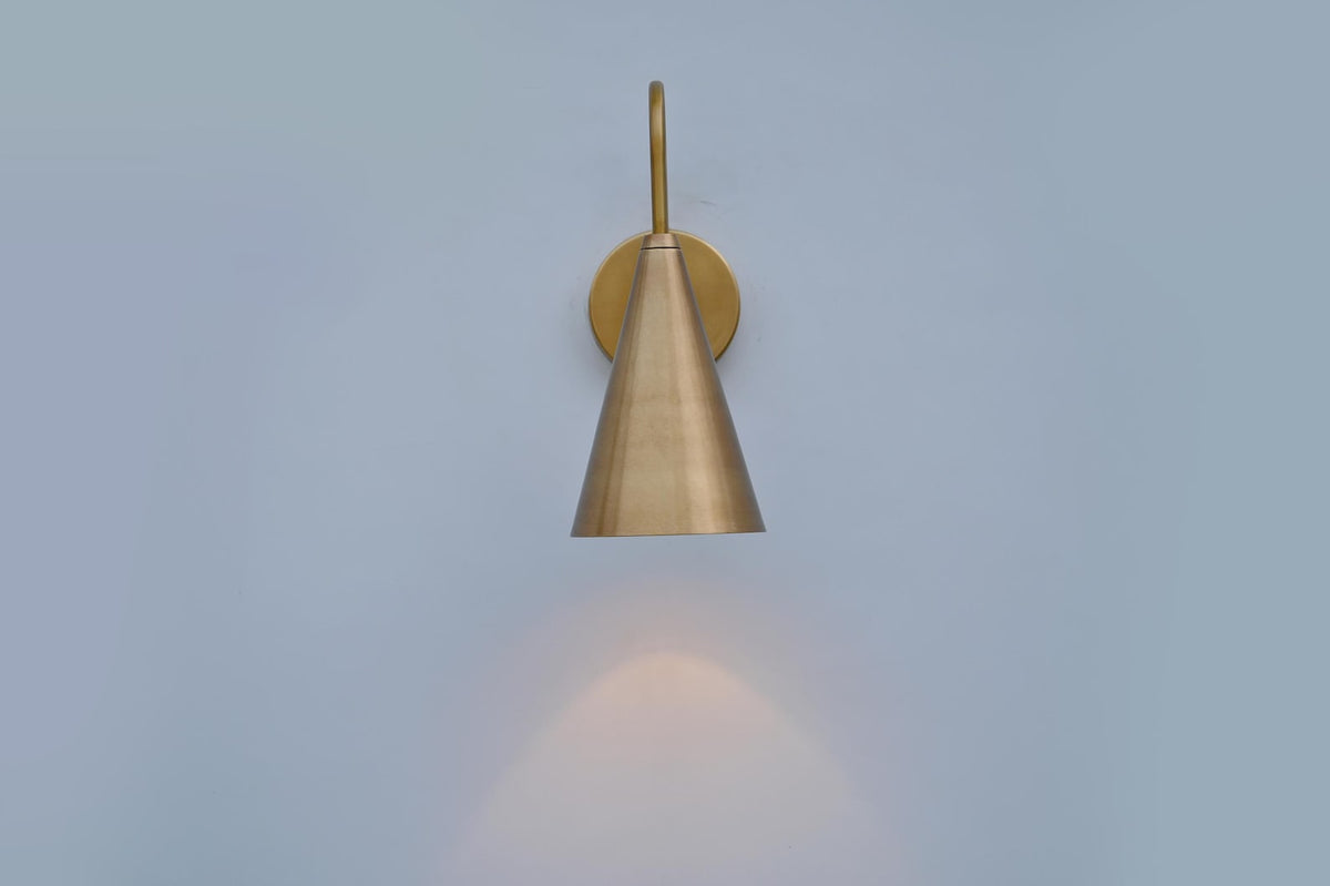 Front view of brass cone-shaped wall sconce casting warm downward light, crafted in brushed satin brass finish.