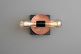 Minimal modern wall light with copper round disc on black square plate and two horizontal filament bulbs, contemporary industrial sconce.