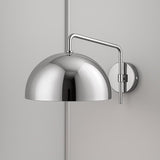 Mirror-finish chrome dome wall sconce with chrome arm and round backplate on a light gray wall.