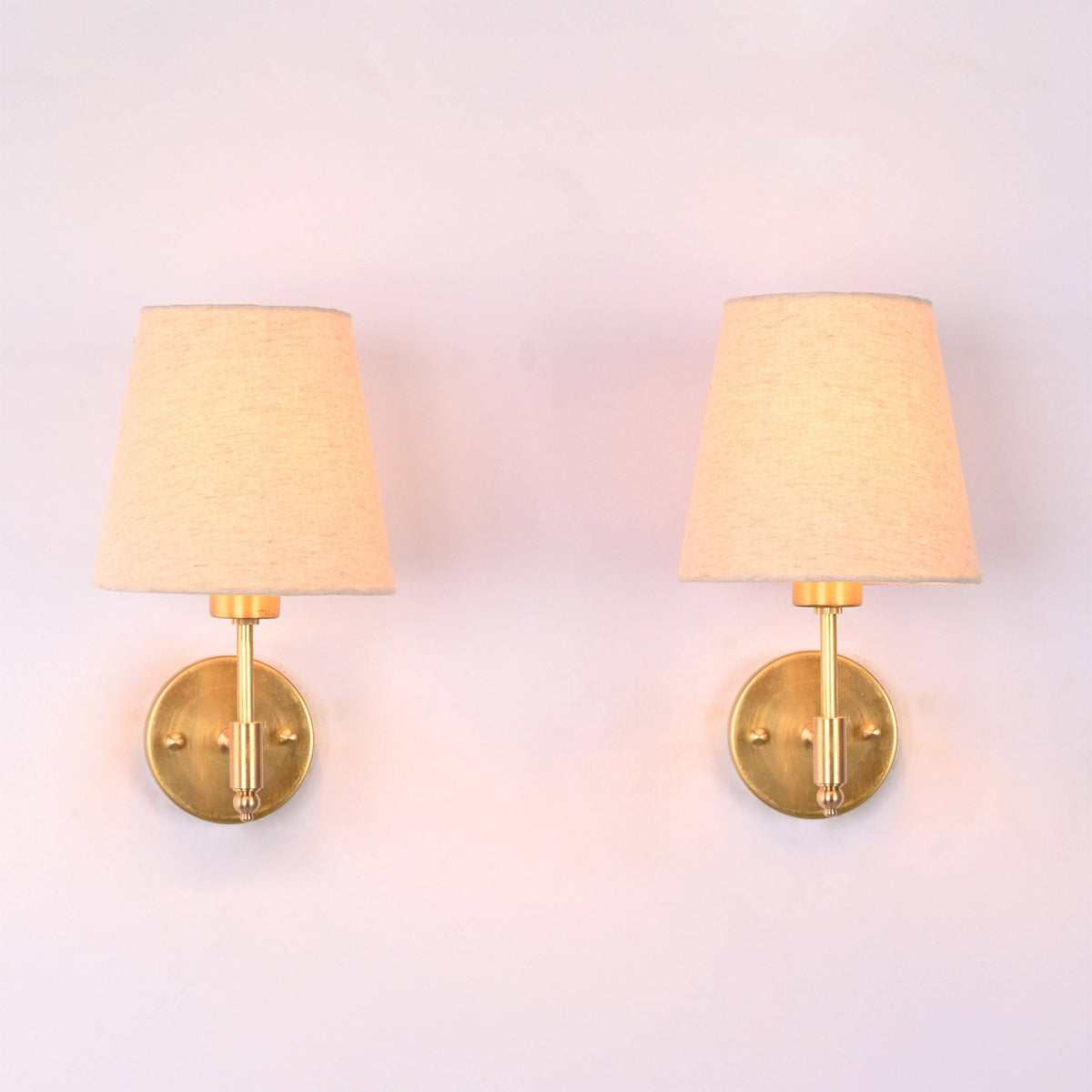 Milan natural linen shade brushed brass short wall sconce with handcrafted solid brass frame and tapered fabric shade, front view.