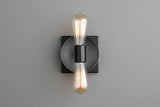 Modern wall sconce with dark graphite round disc on black square backplate and two vertical Edison filament bulbs, minimalist wall lighting.