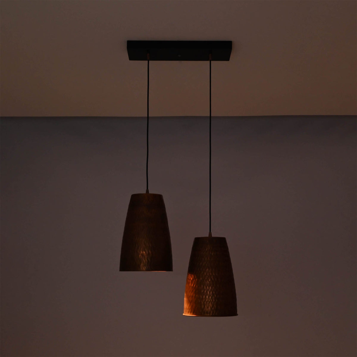 Hudson handcrafted copper dual cone pendant light illuminated with warm ambient lighting highlighting the textured metal finish.