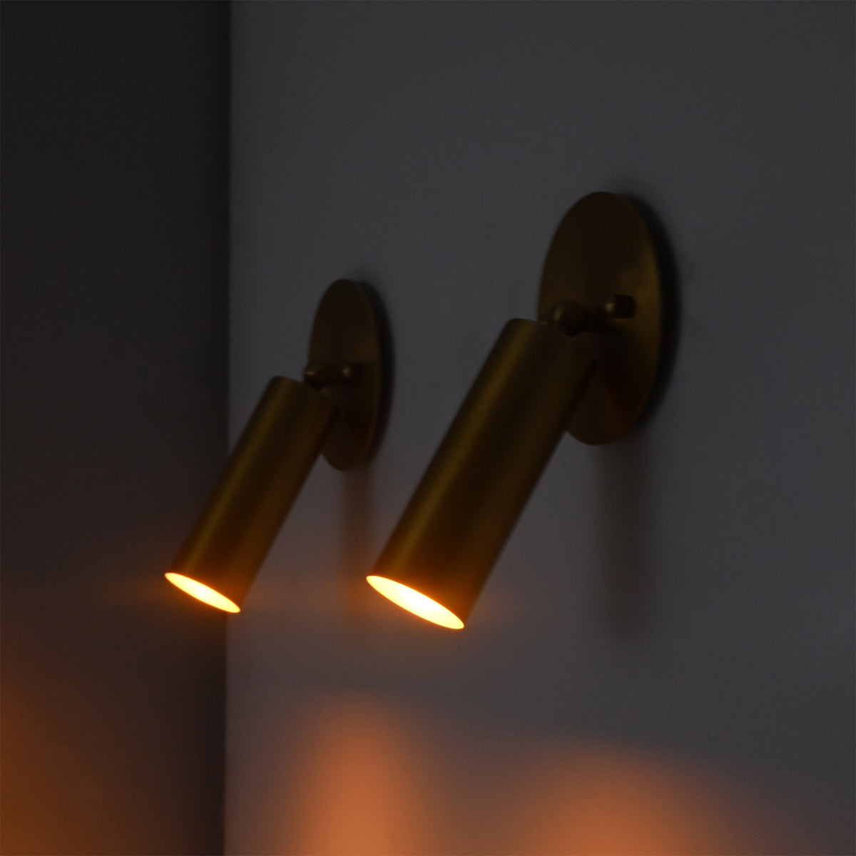 Close-up of two Hudson Modern Brass Adjustable Cylinder Wall Sconces casting warm focused beams to demonstrate their directional task and accent lighting performance.
