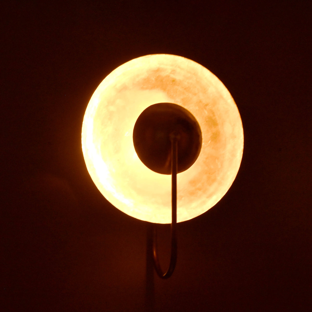 Brass wall sconce glowing warmly in the dark, round shade with radiant halo ambient effect