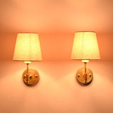 Illuminated Milan brushed brass wall sconces with natural linen fabric shades creating a warm ambient glow.