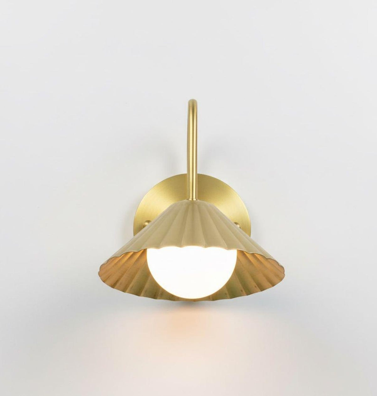 Profile view of brushed brass wall mounted sconce with fluted shade and round backplate