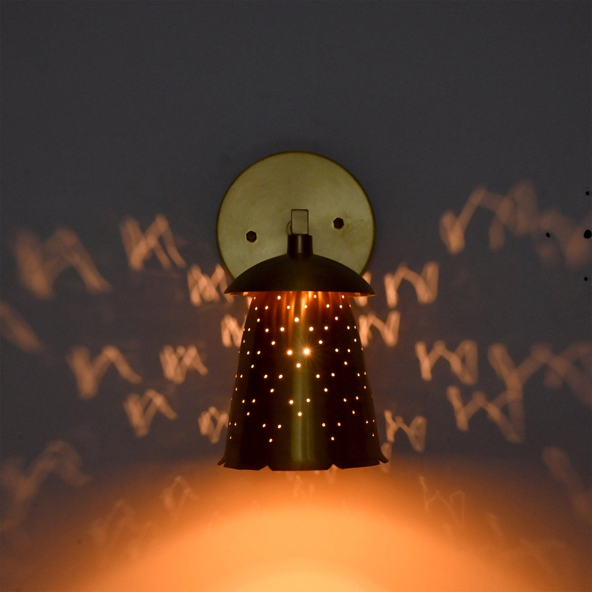 : Luna perforated bell wall sconce glowing warmly with dotted light patterns across the surrounding wall.
