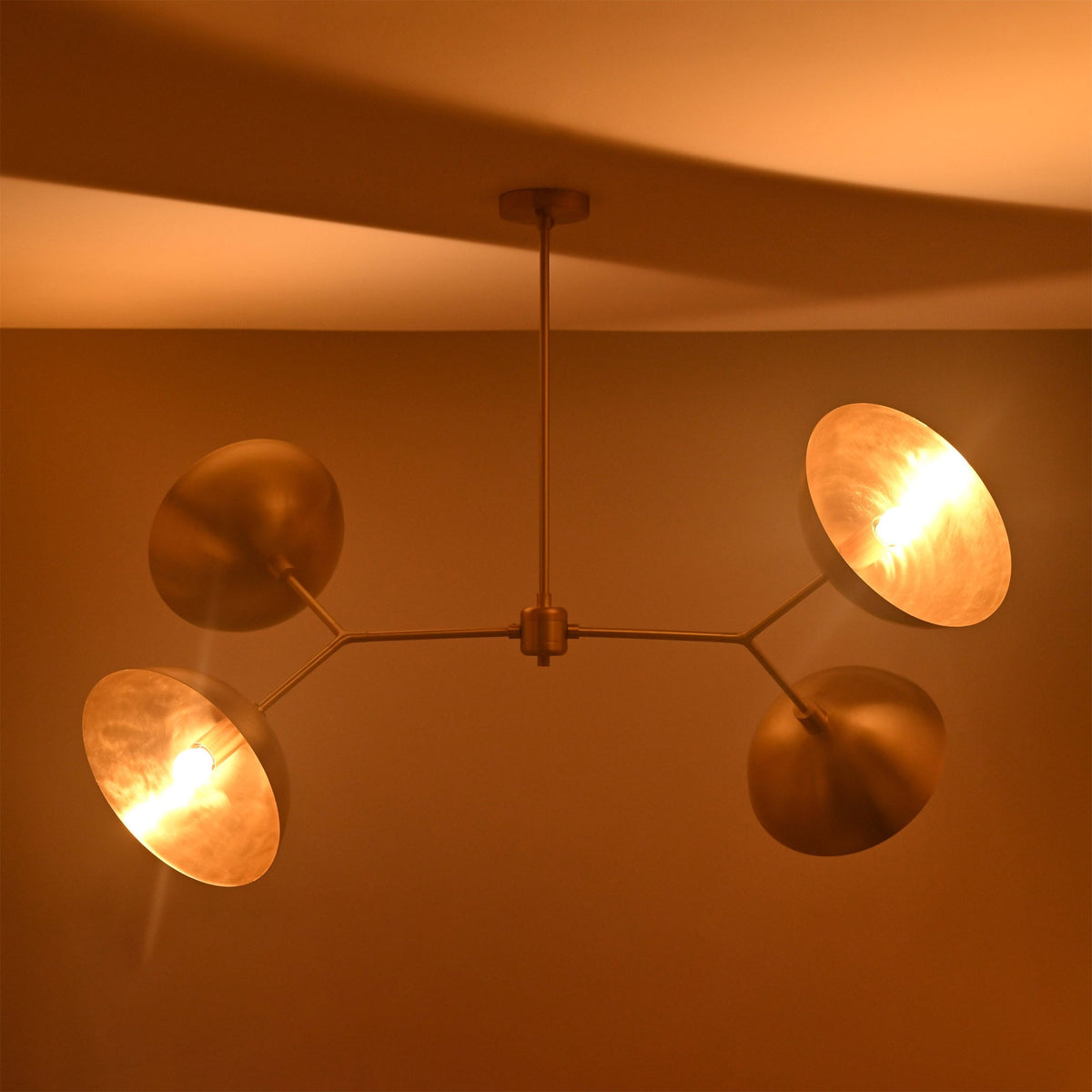 Four-light Madrid Orbital Chandelier with angled disc shades, warm glowing bulbs, and sculptural balanced arm design.