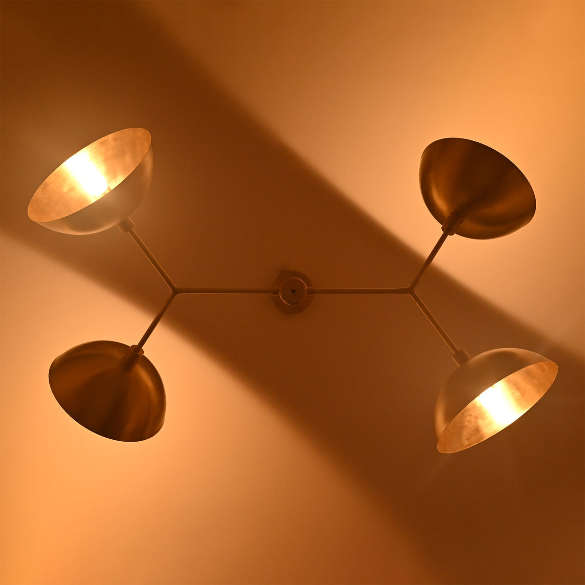 Close-up ceiling view of four-light orbital chandelier with warm bulbs and sculptural disc shade arrangement.