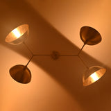 Close-up ceiling view of four-light orbital chandelier with warm bulbs and sculptural disc shade arrangement.