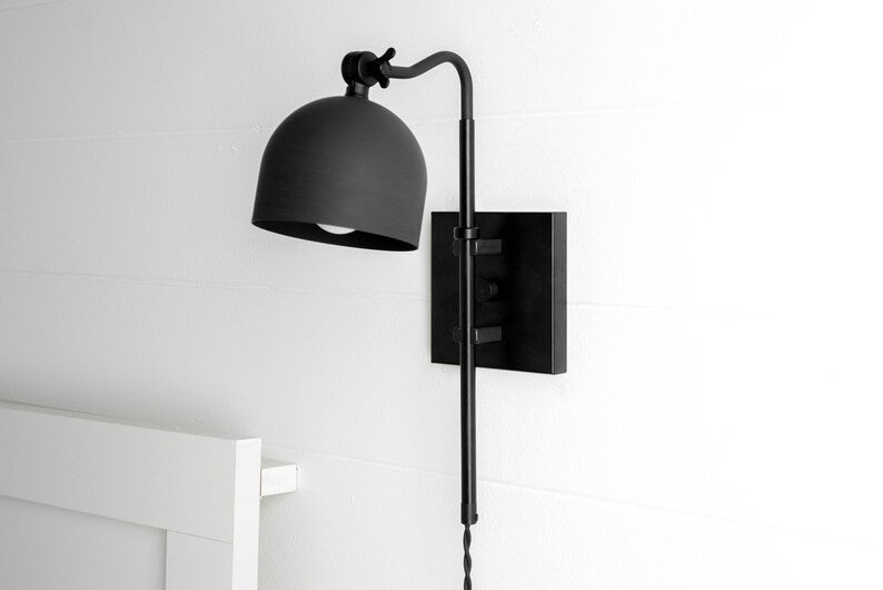 Matte black adjustable wall sconce with dome metal shade and swing arm, modern bedside reading light mounted on white wall