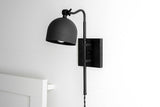 Matte black adjustable wall sconce with dome metal shade and swing arm, modern bedside reading light mounted on white wall