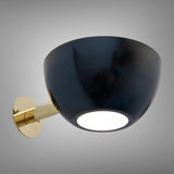 Black bowl wall sconce with polished brass arm turned on, showing a soft diffused light from the bottom opening.