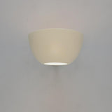 White bowl wall sconce mounted on a gray wall, emitting a soft downward glow from the bottom opening.