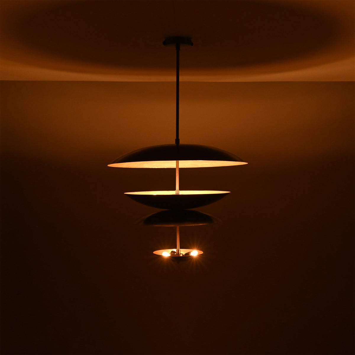 Noir Tiered Disc Chandelier displayed in a dark setting with warm lower bulbs and ambient glow.