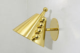 Angled view of polished brass cone wall sconce showing the round backplate, arm connection, and ball accent row.