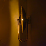 Slim side profile view of brass wall sconce illuminated in low light, highlighting circular glow effect