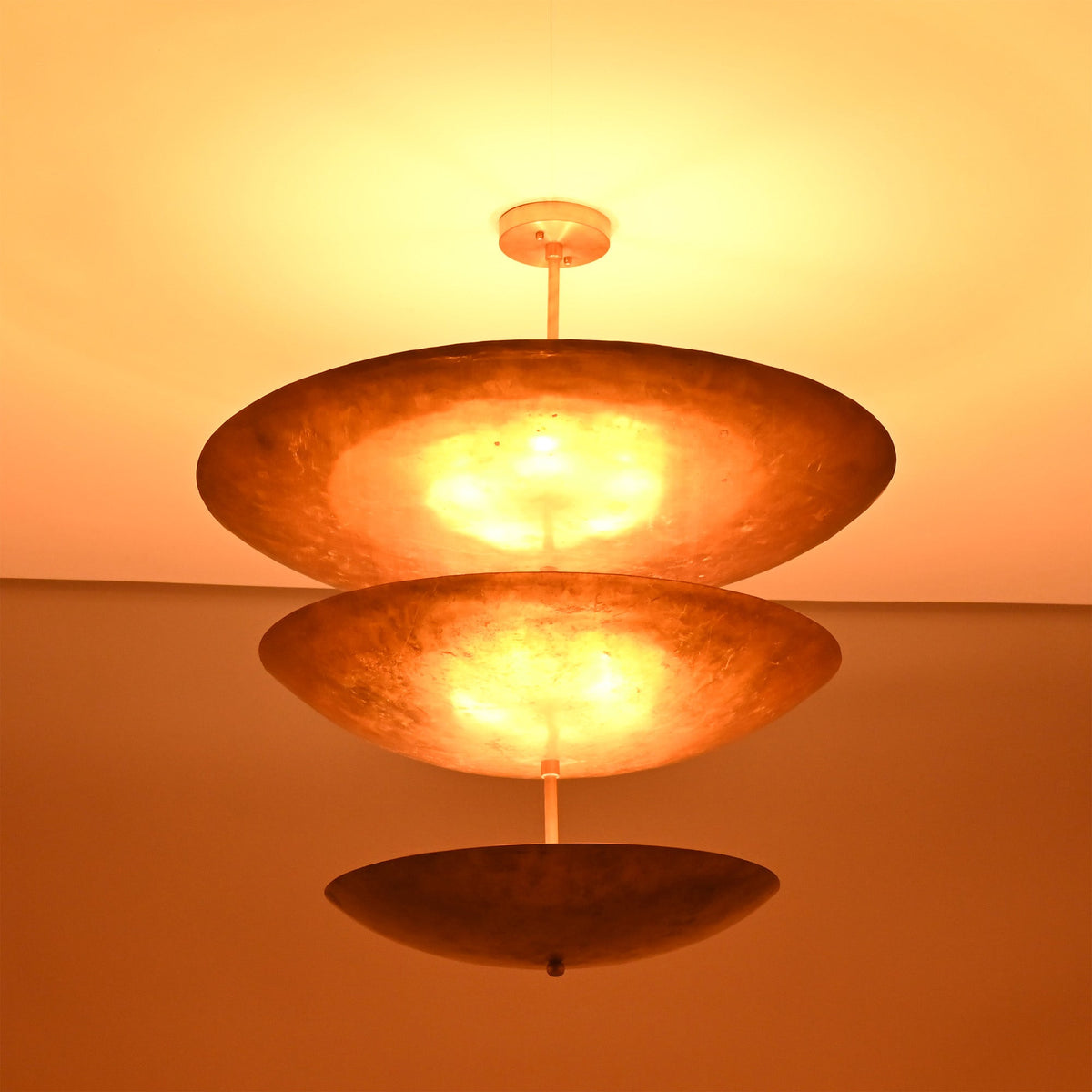 Siena Three Tier Disc Chandelier illuminated from below, highlighting its warm glow and dramatic layered ceiling profile.
