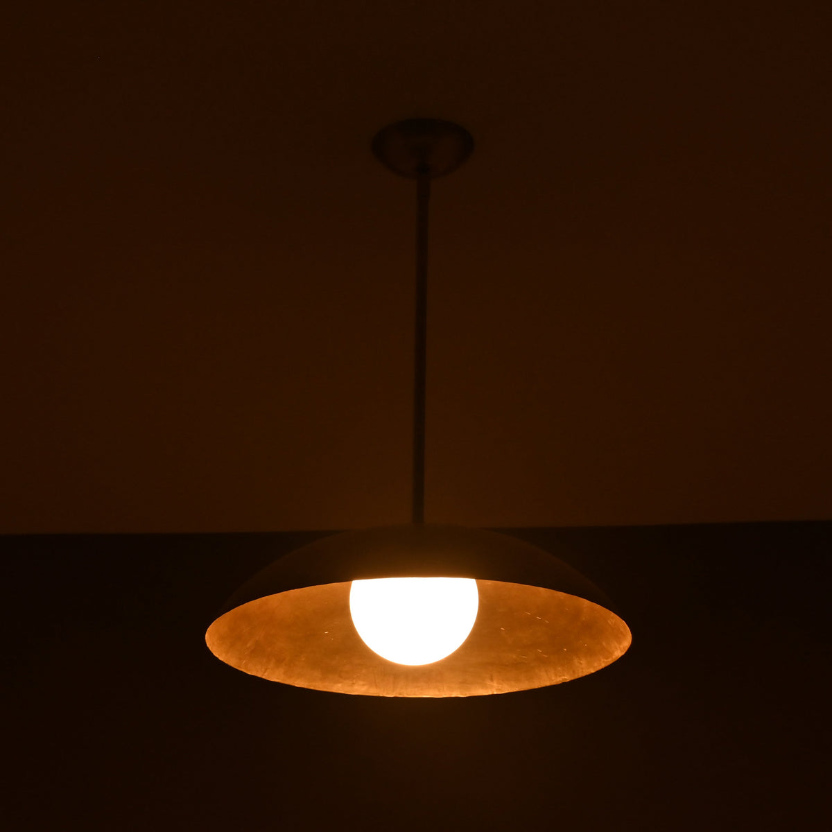 Wide view of lit brass pendant light casting ambient golden light, handmade by Brass Leaf Studio
