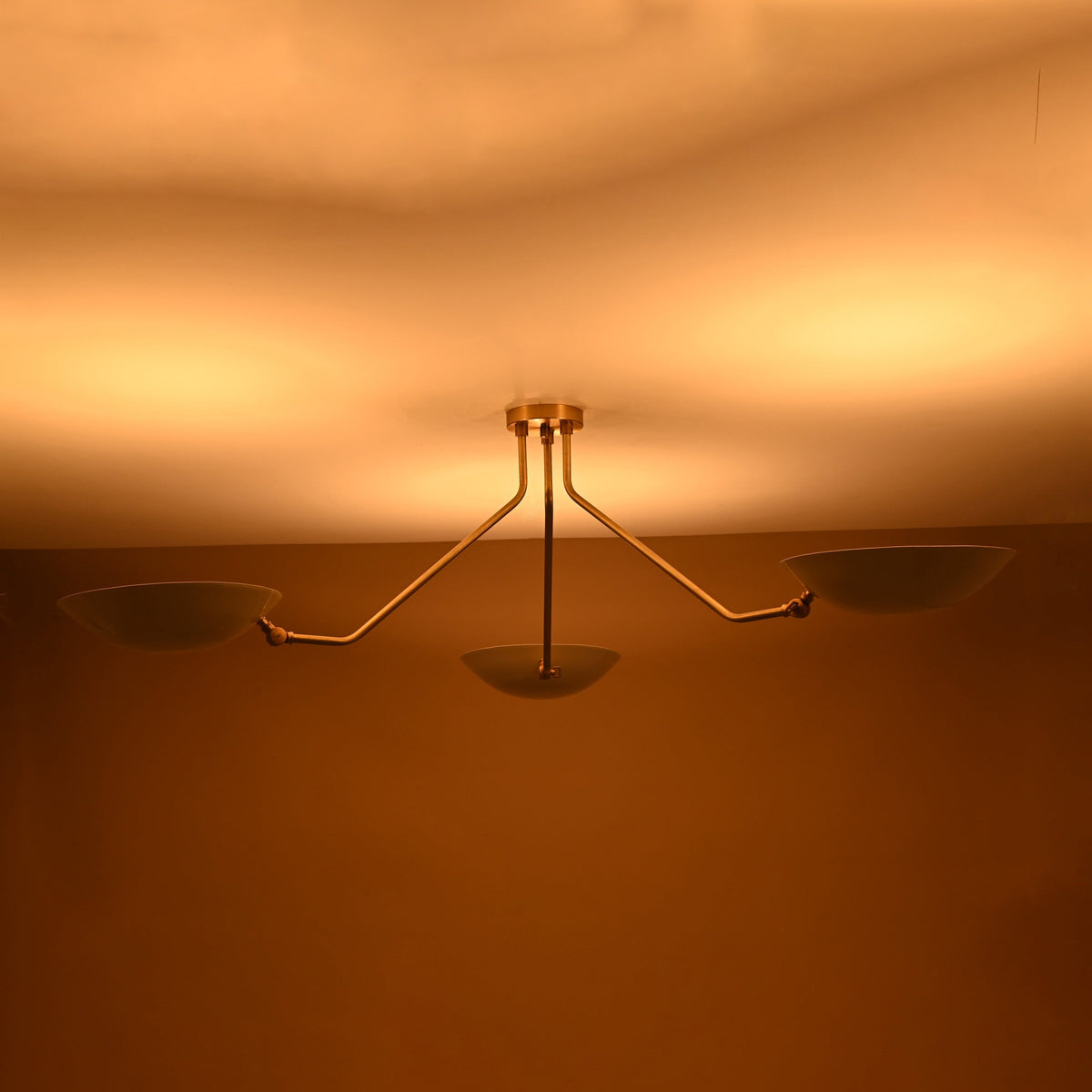 Contemporary three-light brass chandelier emitting soft indirect lighting with white enamel shades