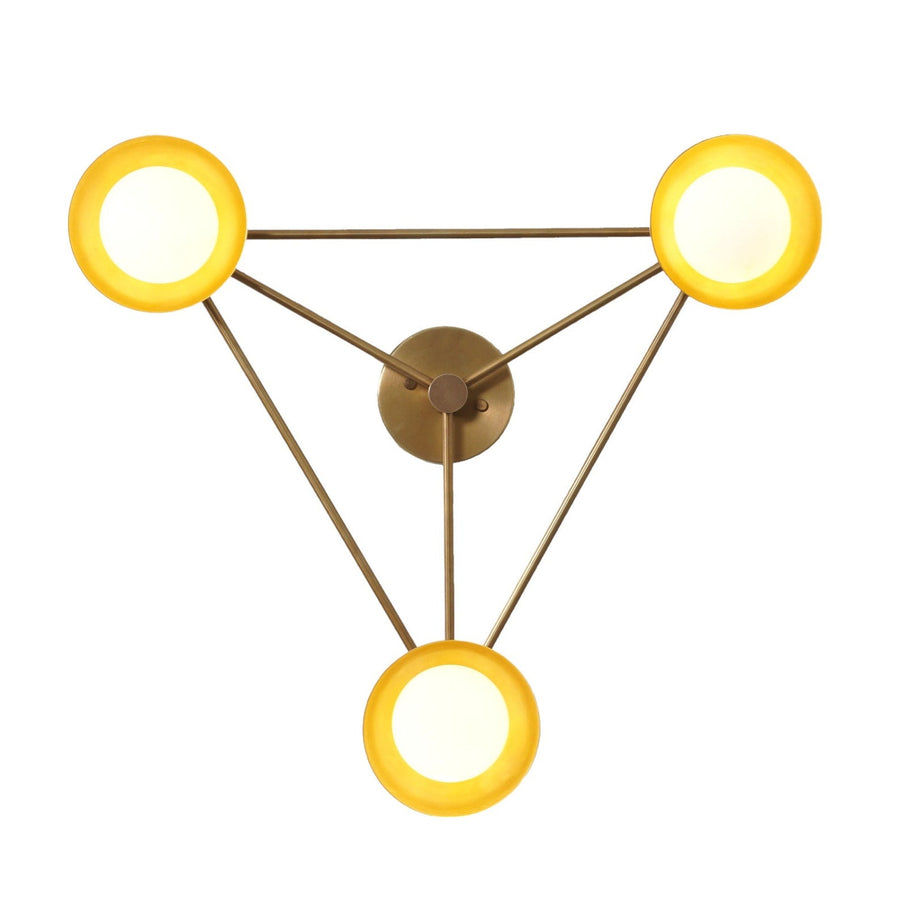 Modern brass wall lamp featuring three circular disc shades arranged in a triangular form, emitting a warm ambient glow for elegant wall lighting.
