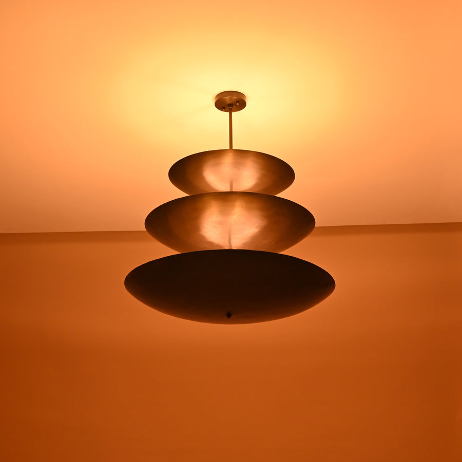 Three-layer brass chandelier in blackened finish viewed from side, minimalist industrial ceiling light