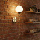 Lit Verona globe balance wall sconce with warm glowing glass globe and elegant antique brass frame.