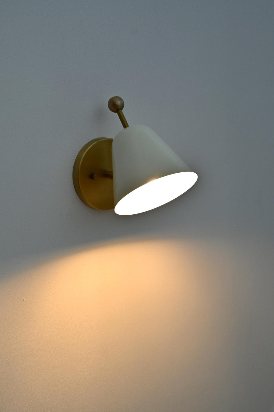 Minimalist white shade brass wall sconce angled view with round backplate and conical shade.