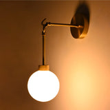 Side view of the Windsor Modern Brass Globe Wall Sconce installed on a wall, showcasing its decorative brass arm, suspended globe, and warm ambient glow.