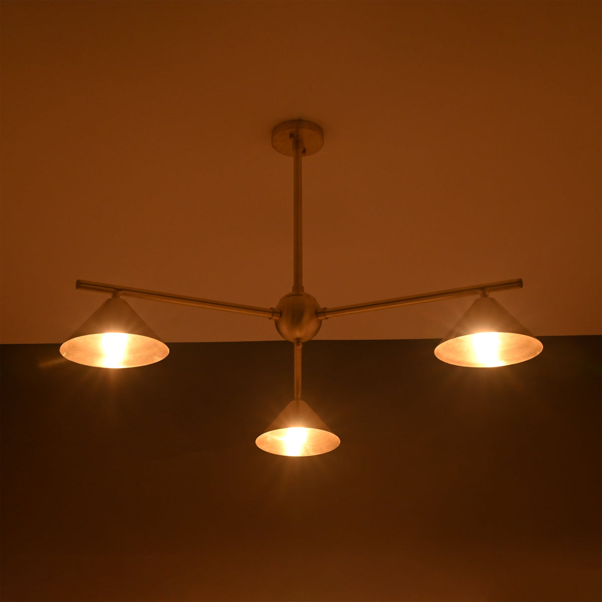 Minimalist brass chandelier glowing warmly at night, with sculpted cone shades creating soft ambient illumination.