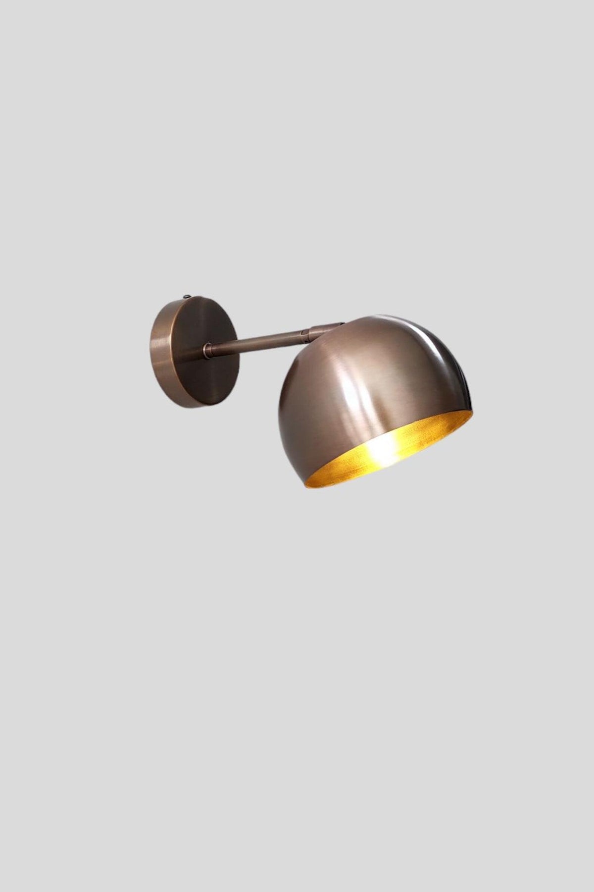 Illuminated antique patina brass wall sconce featuring bowl-shaped shade and warm ambient glow