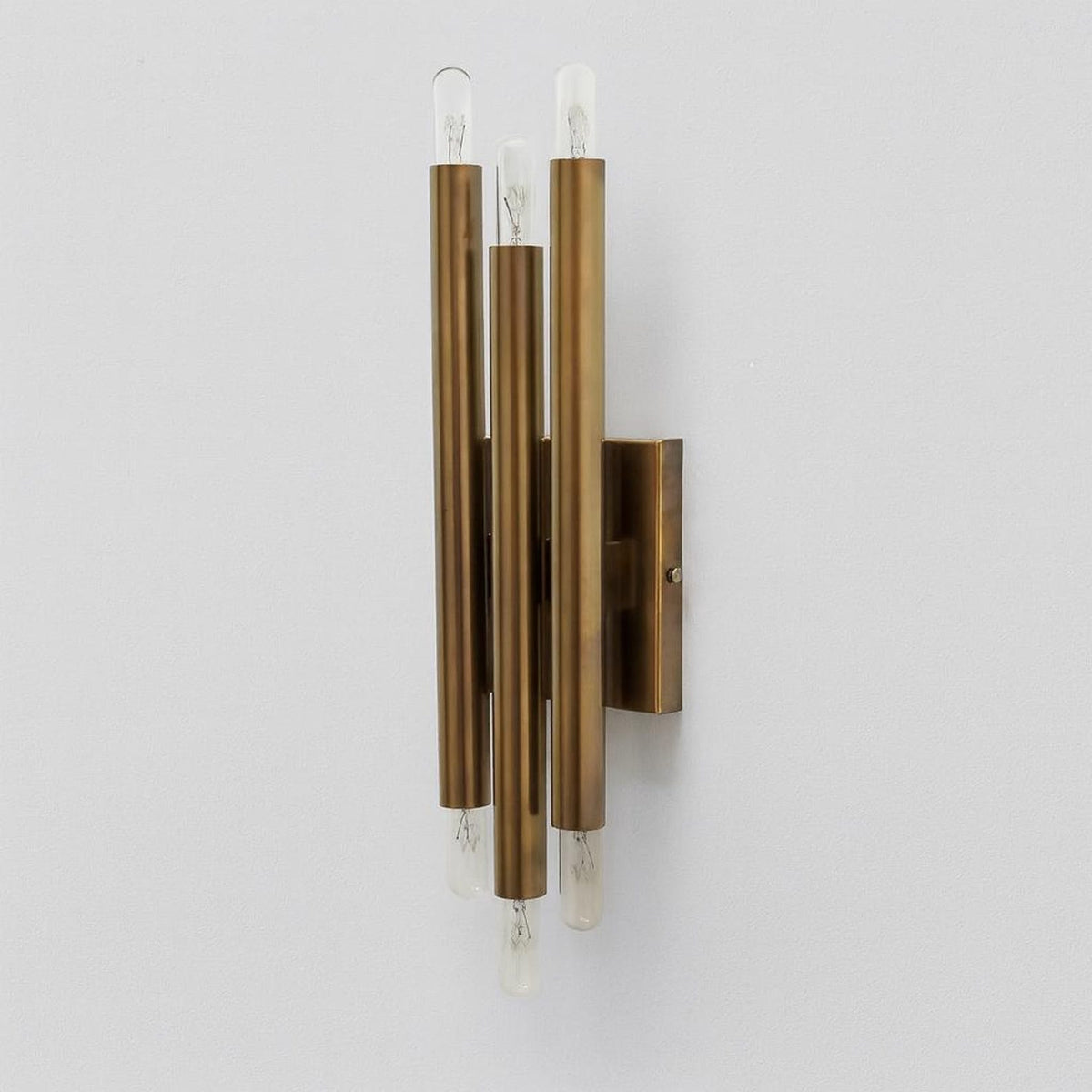 Architectural brass wall light with six vertical tubes and industrial exposed bulbs mounted on rectangular brass backplate