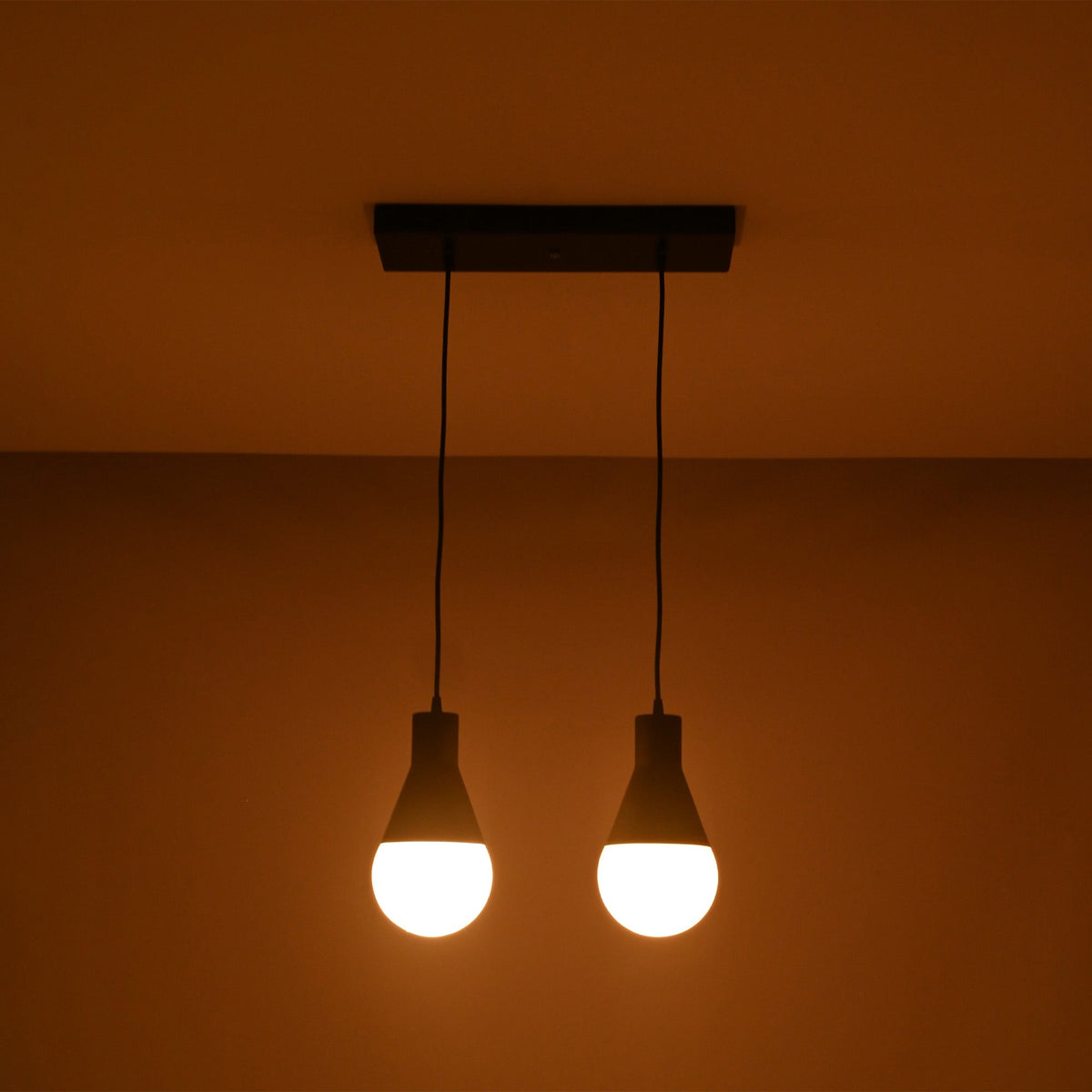 Angled illuminated view of the Aspen Dual Socket Pendant Chandelier with two glowing globe bulbs in a modern minimalist design.