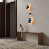 Closeup of backlit blue disc wall sconce showing warm ambient glow and sculptural brass detailing