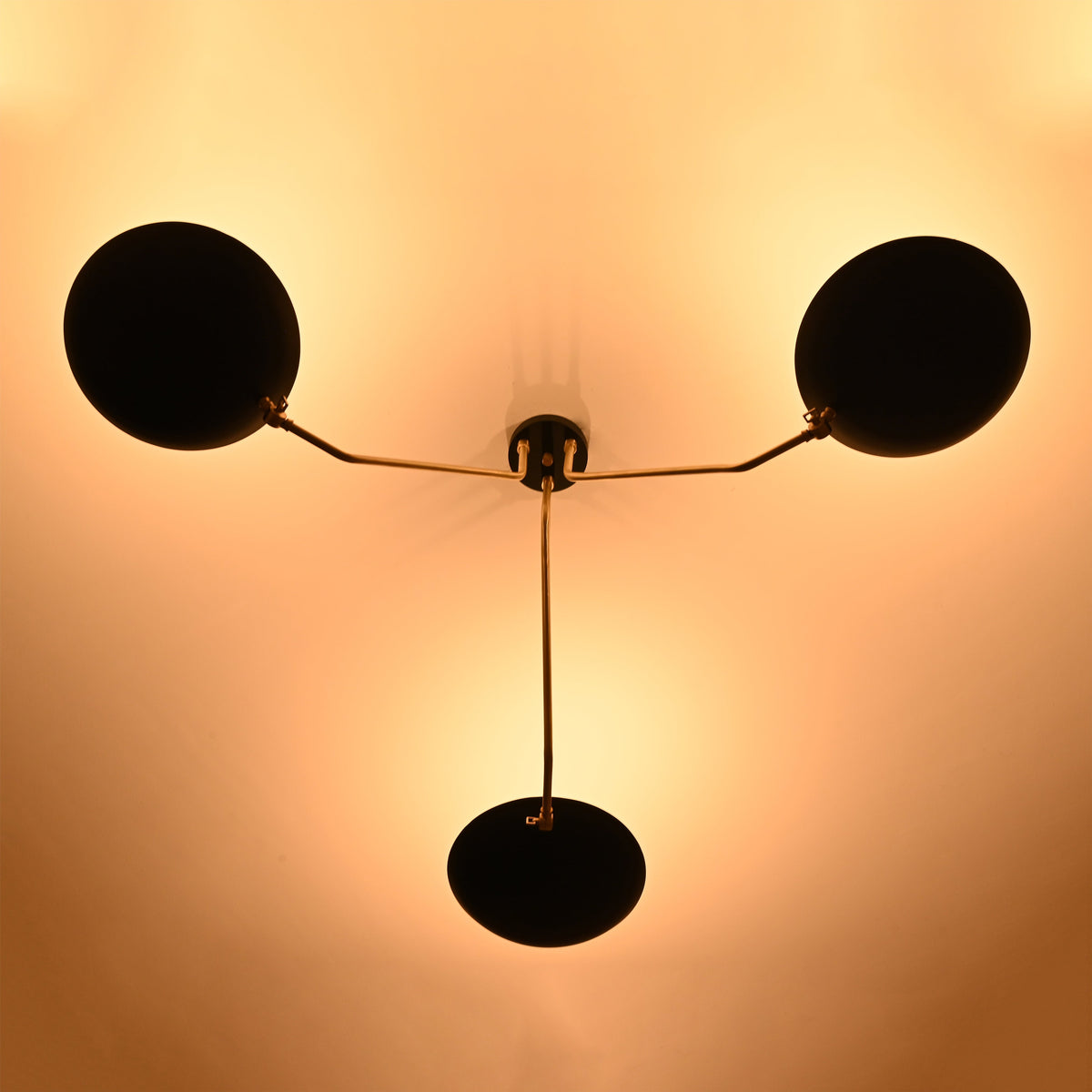 Bottom glowing view of black bowl chandelier illuminating the ceiling with warm ambient light and stylish brass arms.